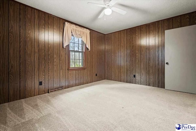 unfurnished room with carpet floors, wooden walls, and ceiling fan