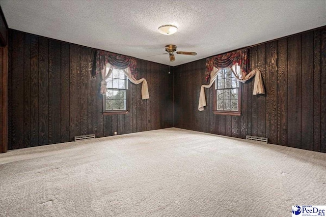 carpeted empty room with ceiling fan, plenty of natural light, wooden walls, and a textured ceiling