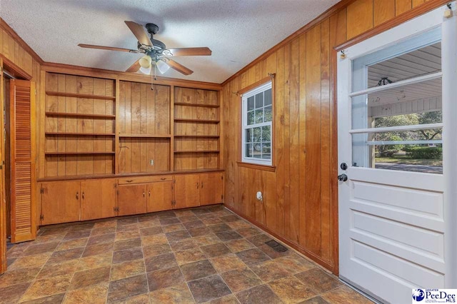 interior space with crown molding, ceiling fan, a textured ceiling, and wood walls