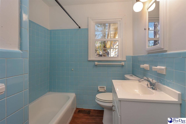 full bathroom featuring washtub / shower combination, tile walls, hardwood / wood-style floors, vanity, and toilet