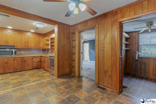 kitchen with sink, tasteful backsplash, appliances with stainless steel finishes, wooden walls, and ceiling fan