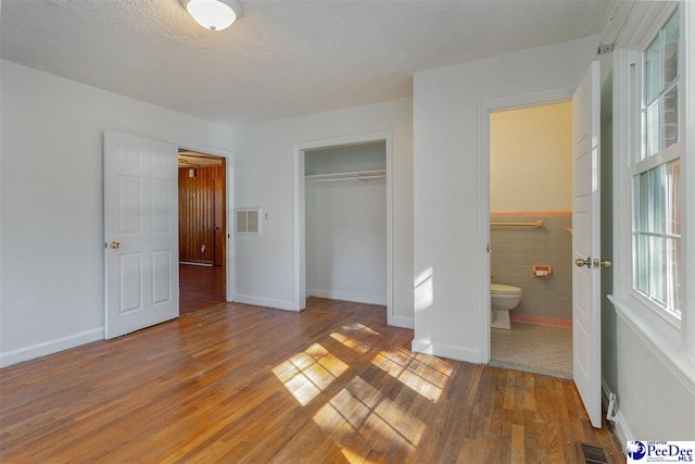 unfurnished bedroom with a closet, hardwood / wood-style floors, a textured ceiling, and tile walls