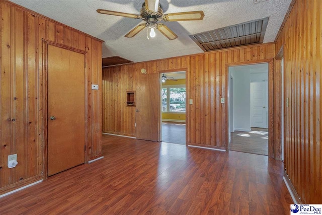 unfurnished room featuring ceiling fan, wood-type flooring, a textured ceiling, and wood walls