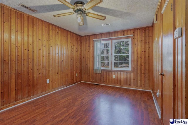 spare room featuring wooden walls, ceiling fan, dark hardwood / wood-style floors, and a textured ceiling