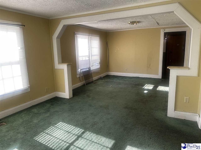 spare room featuring crown molding, a textured ceiling, dark carpet, and a wealth of natural light