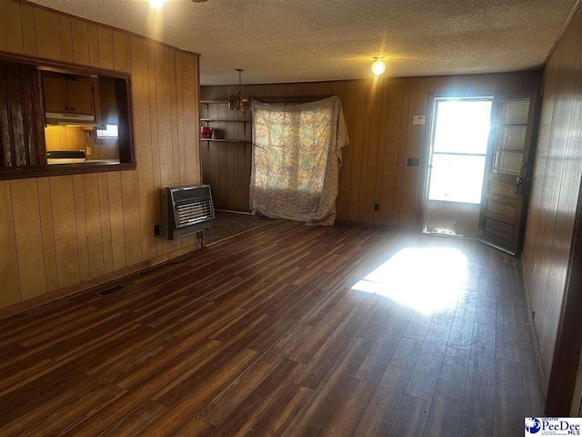 spare room with dark wood-style floors, heating unit, visible vents, wooden walls, and a textured ceiling