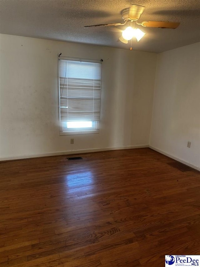 empty room featuring dark wood-style floors, visible vents, ceiling fan, a textured ceiling, and baseboards