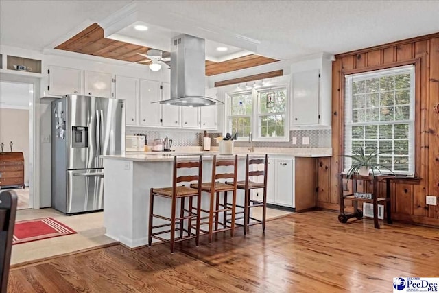 kitchen featuring island range hood, white cabinets, light wood-type flooring, and stainless steel fridge with ice dispenser