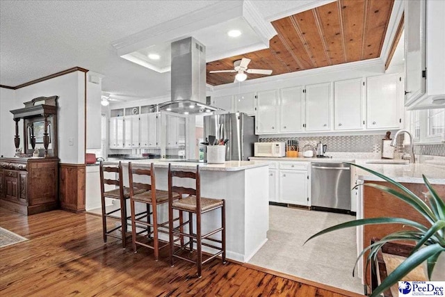 kitchen with sink, ornamental molding, island exhaust hood, stainless steel appliances, and white cabinets