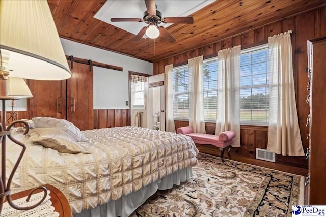 bedroom with wood ceiling, wooden walls, and a barn door