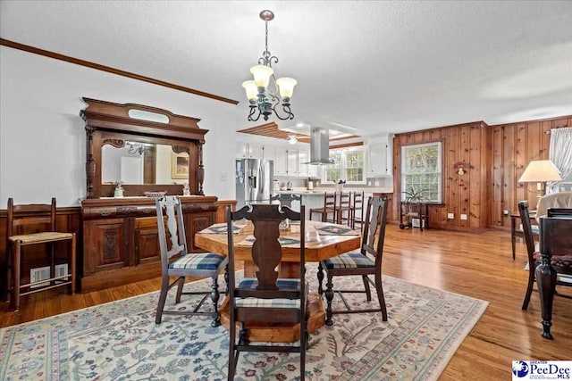 dining space with a notable chandelier, wood walls, a textured ceiling, and light wood-type flooring