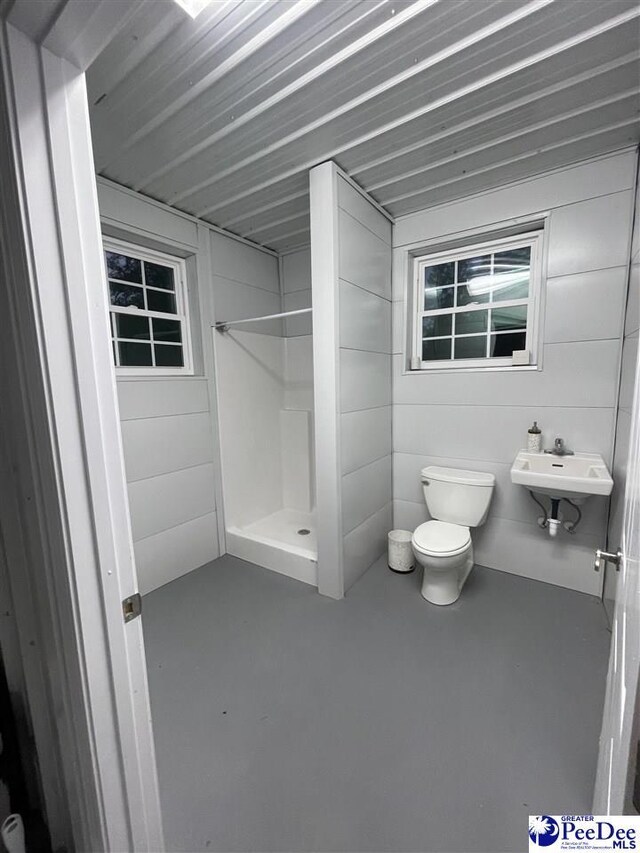 bathroom featuring concrete flooring, a shower, sink, and toilet