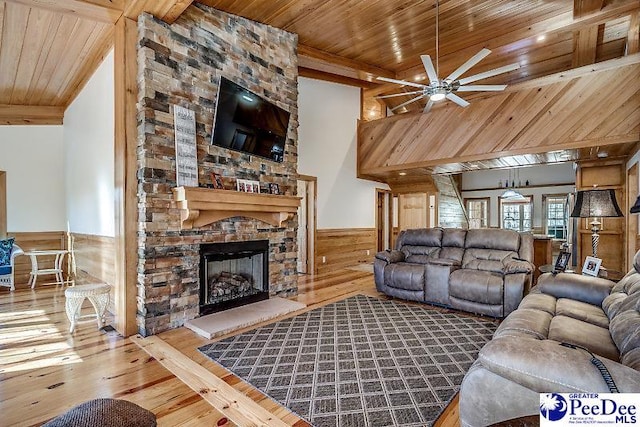 living room featuring ceiling fan, wood-type flooring, a stone fireplace, wooden ceiling, and wood walls