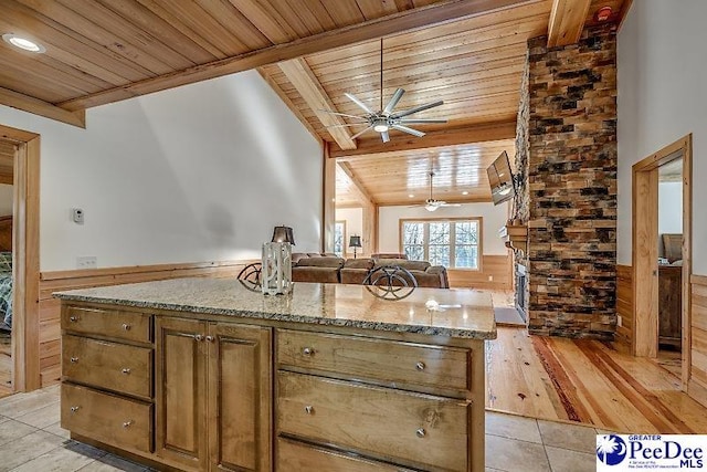 kitchen featuring wood ceiling, ceiling fan, a center island, lofted ceiling with beams, and light stone countertops