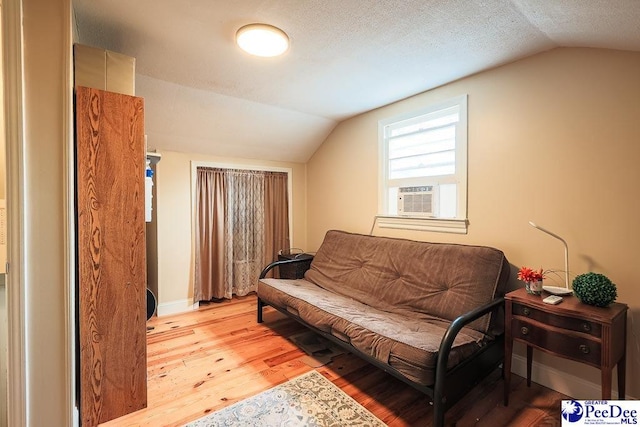 sitting room featuring lofted ceiling, cooling unit, light wood-style flooring, and a textured ceiling