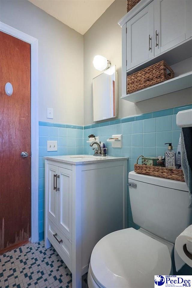 bathroom featuring tile walls, toilet, wainscoting, vanity, and tile patterned floors