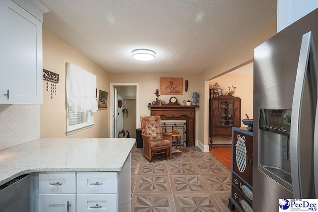 kitchen featuring light stone counters, decorative backsplash, appliances with stainless steel finishes, white cabinetry, and a textured ceiling