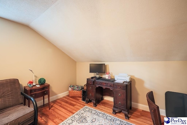 home office featuring light wood-type flooring, vaulted ceiling, a textured ceiling, and baseboards