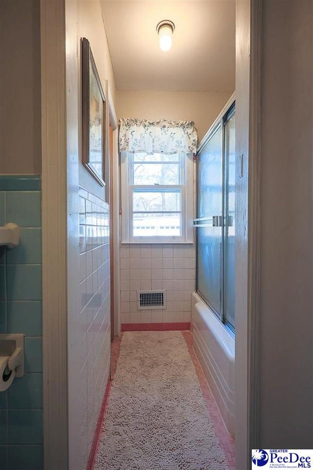 bathroom featuring tile patterned flooring, visible vents, bath / shower combo with glass door, and tile walls