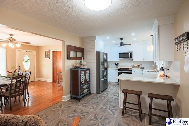 kitchen with a peninsula, stainless steel appliances, a kitchen bar, white cabinetry, and a sink