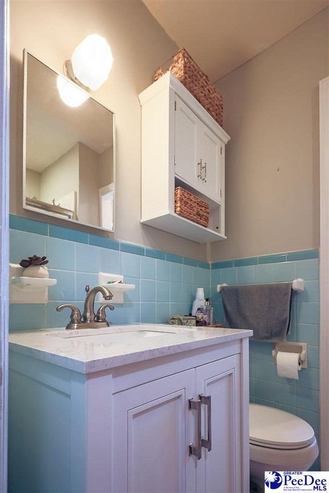 bathroom featuring tile walls, wainscoting, vanity, and toilet