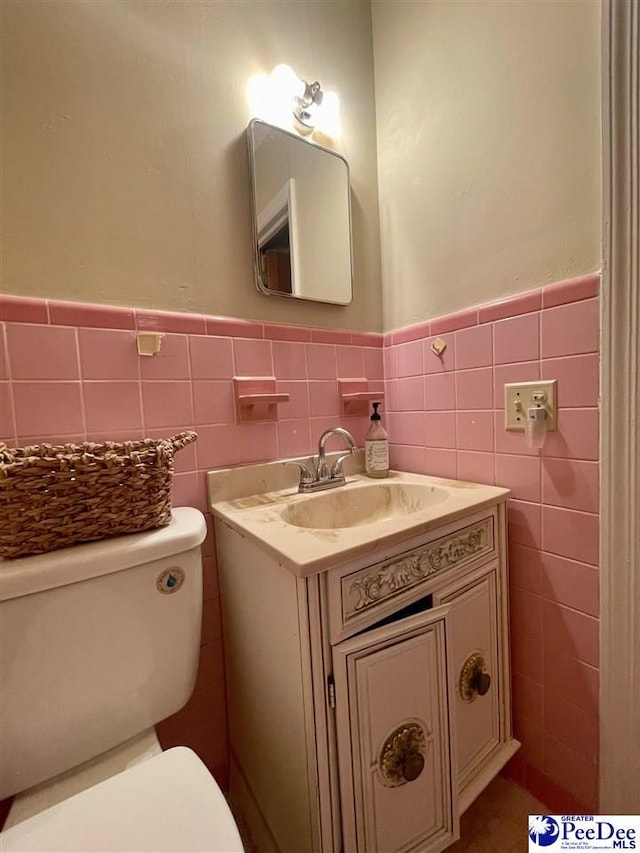 bathroom featuring toilet, wainscoting, tile walls, and vanity