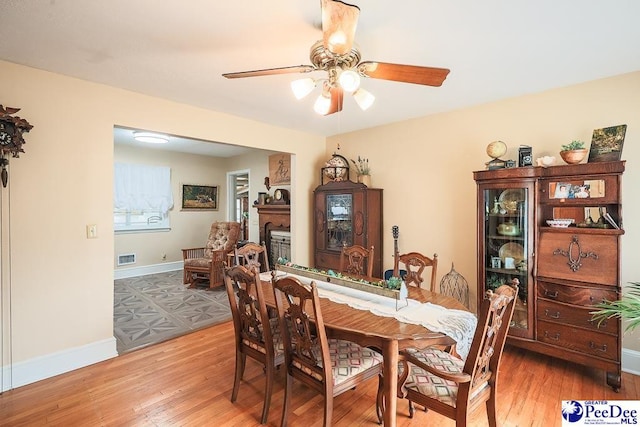 dining room with light wood-style flooring, visible vents, a ceiling fan, baseboards, and a glass covered fireplace