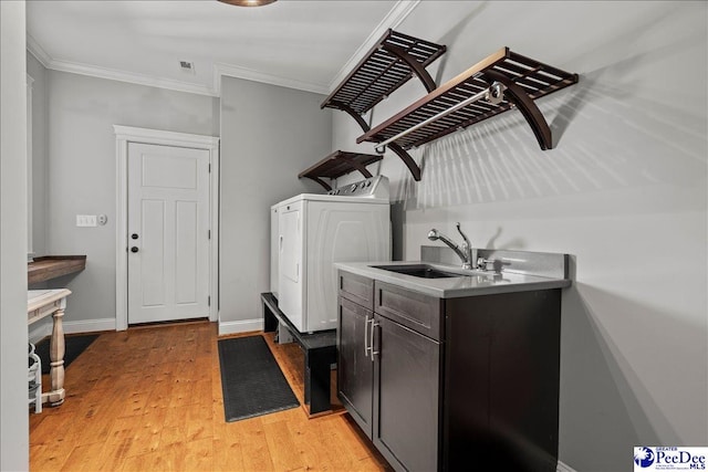 clothes washing area with light wood-style flooring, ornamental molding, washer and clothes dryer, a sink, and cabinet space