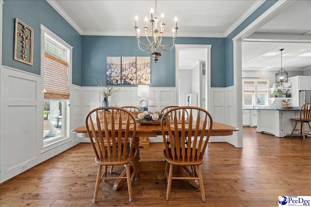 dining room with a notable chandelier, ornamental molding, a wainscoted wall, and hardwood / wood-style floors