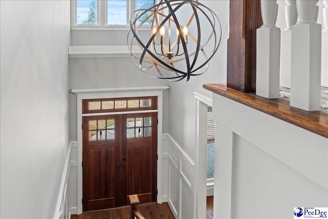 entryway with a notable chandelier, wood finished floors, a wealth of natural light, and wainscoting