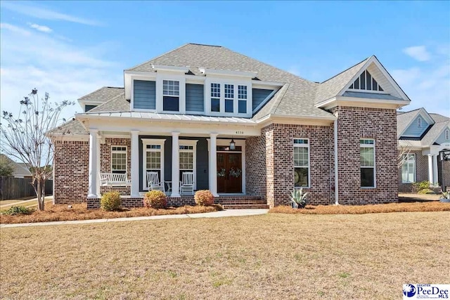 view of front of house featuring brick siding, covered porch, a front lawn, and roof with shingles