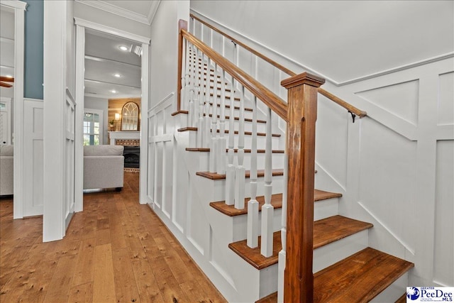 staircase featuring a brick fireplace, hardwood / wood-style floors, crown molding, and a decorative wall