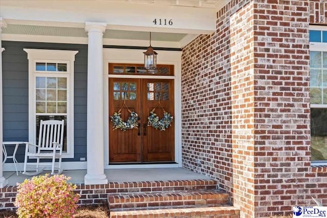 entrance to property featuring a porch and brick siding