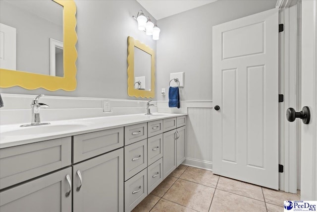 bathroom with a sink, double vanity, wainscoting, and tile patterned floors