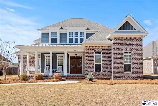 view of front of house with a standing seam roof, covered porch, roof with shingles, metal roof, and brick siding