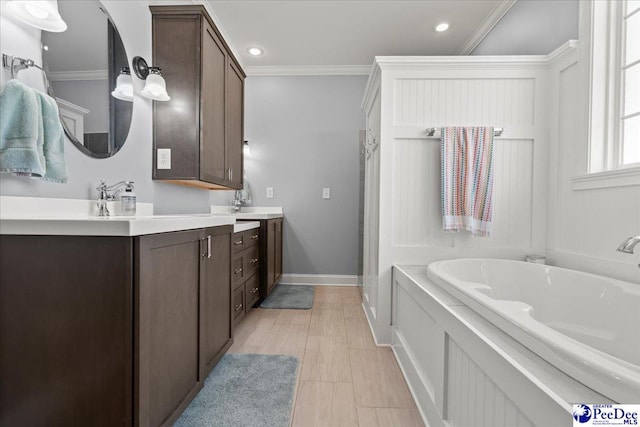 bathroom with a garden tub, ornamental molding, recessed lighting, baseboards, and vanity