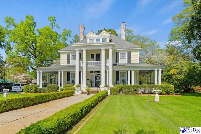 neoclassical / greek revival house featuring a porch, a chimney, a balcony, and a front yard