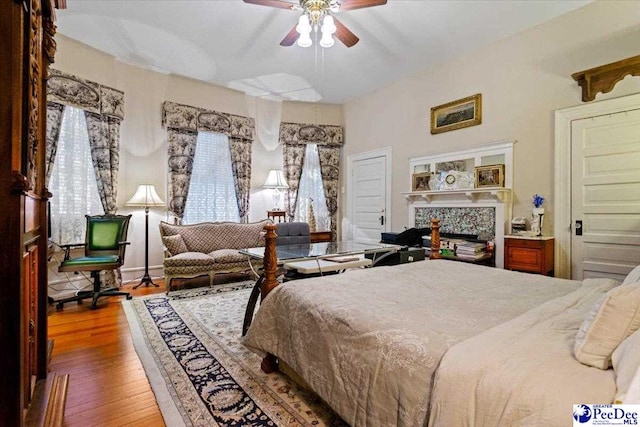 bedroom featuring ceiling fan, hardwood / wood-style flooring, and a premium fireplace