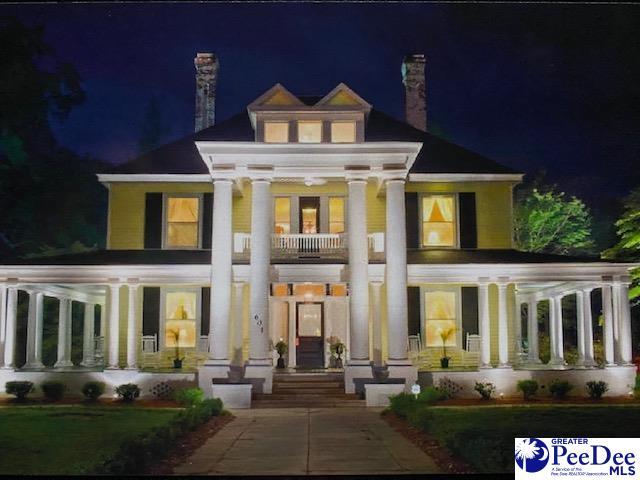 back of house at twilight featuring covered porch, a chimney, and a balcony