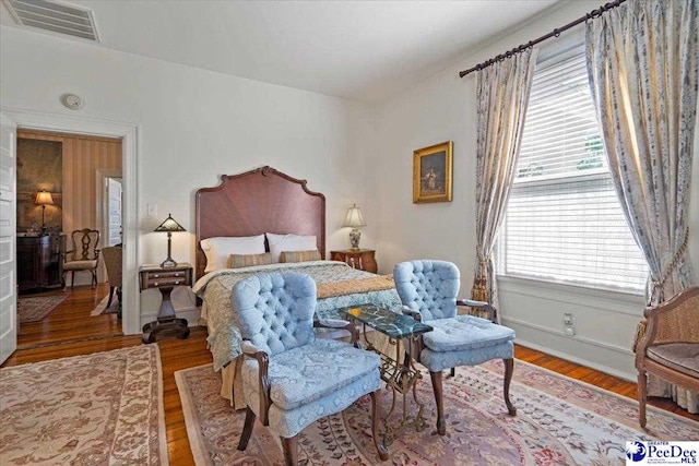 bedroom with visible vents, baseboards, wood finished floors, and multiple windows