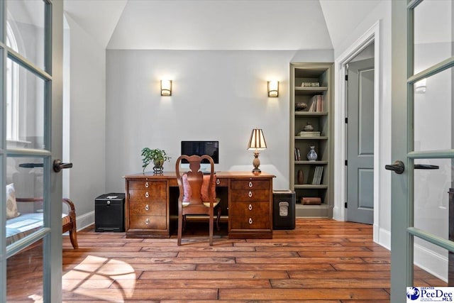 office space featuring lofted ceiling, built in shelves, and light wood-type flooring