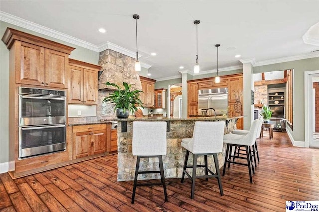 kitchen with appliances with stainless steel finishes, a kitchen breakfast bar, an island with sink, pendant lighting, and light stone countertops