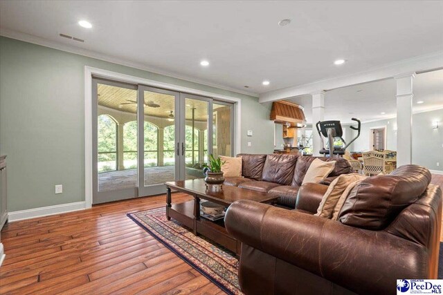 living room with decorative columns, crown molding, light wood-type flooring, and french doors