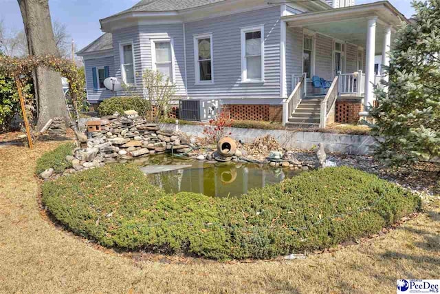 view of front of house with a shingled roof, covered porch, a small pond, and central air condition unit