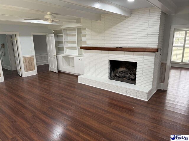 unfurnished living room featuring ceiling fan, beam ceiling, dark hardwood / wood-style flooring, and a brick fireplace