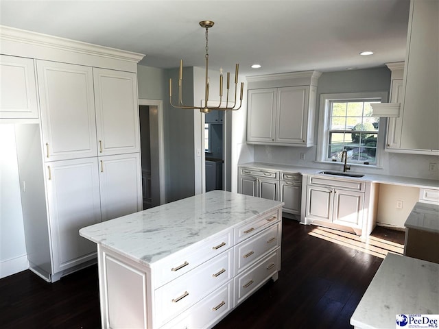 kitchen featuring sink, light stone counters, white cabinetry, decorative light fixtures, and dark hardwood / wood-style floors