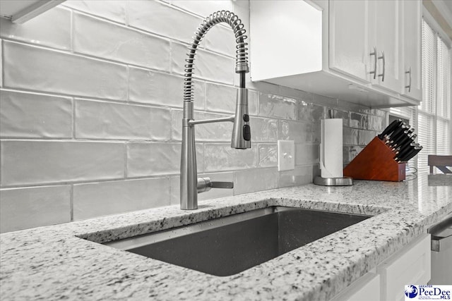 room details featuring a sink, decorative backsplash, light stone counters, and white cabinets