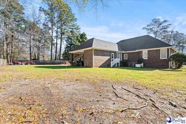 back of property with crawl space, brick siding, a yard, and fence