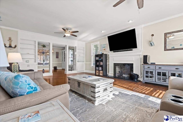 living area with crown molding, built in shelves, wood finished floors, and a fireplace with raised hearth