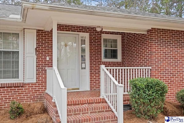 view of exterior entry featuring brick siding and roof with shingles